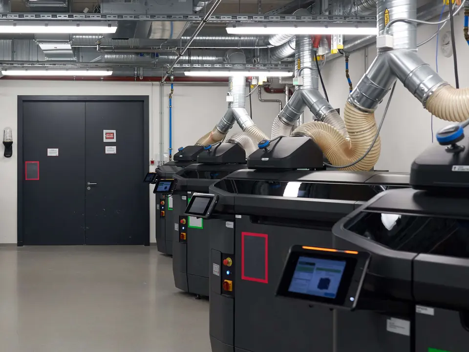 Protolabs production floor: a row of industrial 3D printers under extraction ducting